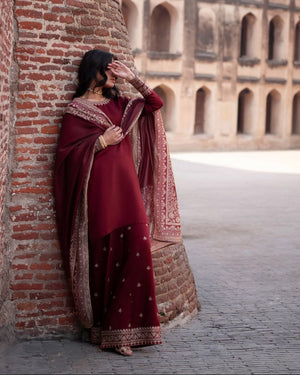 Woman in a red traditional outfit standing in a historical architectural setting with a minaret in the background.