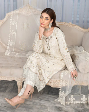 Woman in a white embroidered outfit sitting on a decorative sofa.