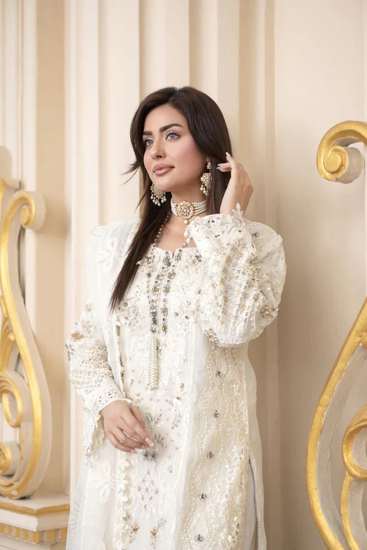 Woman in a white dress with intricate details against a decorative wall.
