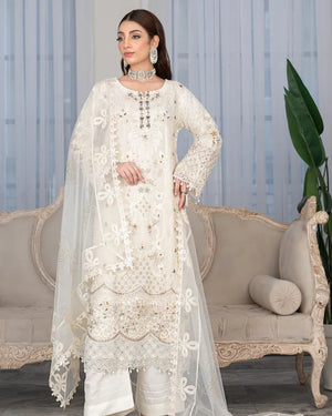 Woman in a white embroidered traditional outfit standing in a decorated room with a sofa and plant.
